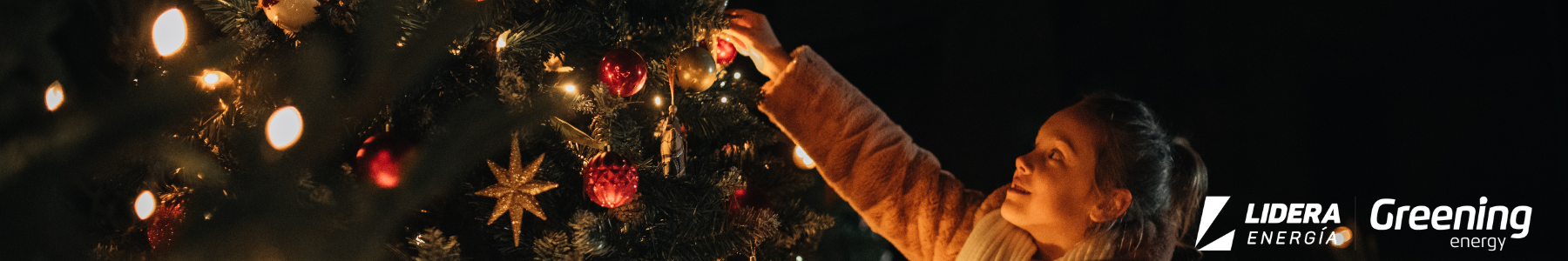 Niña decorando un árbol de Navidad con luces LED, representando el uso de iluminación eficiente para reducir el consumo energético en invierno.